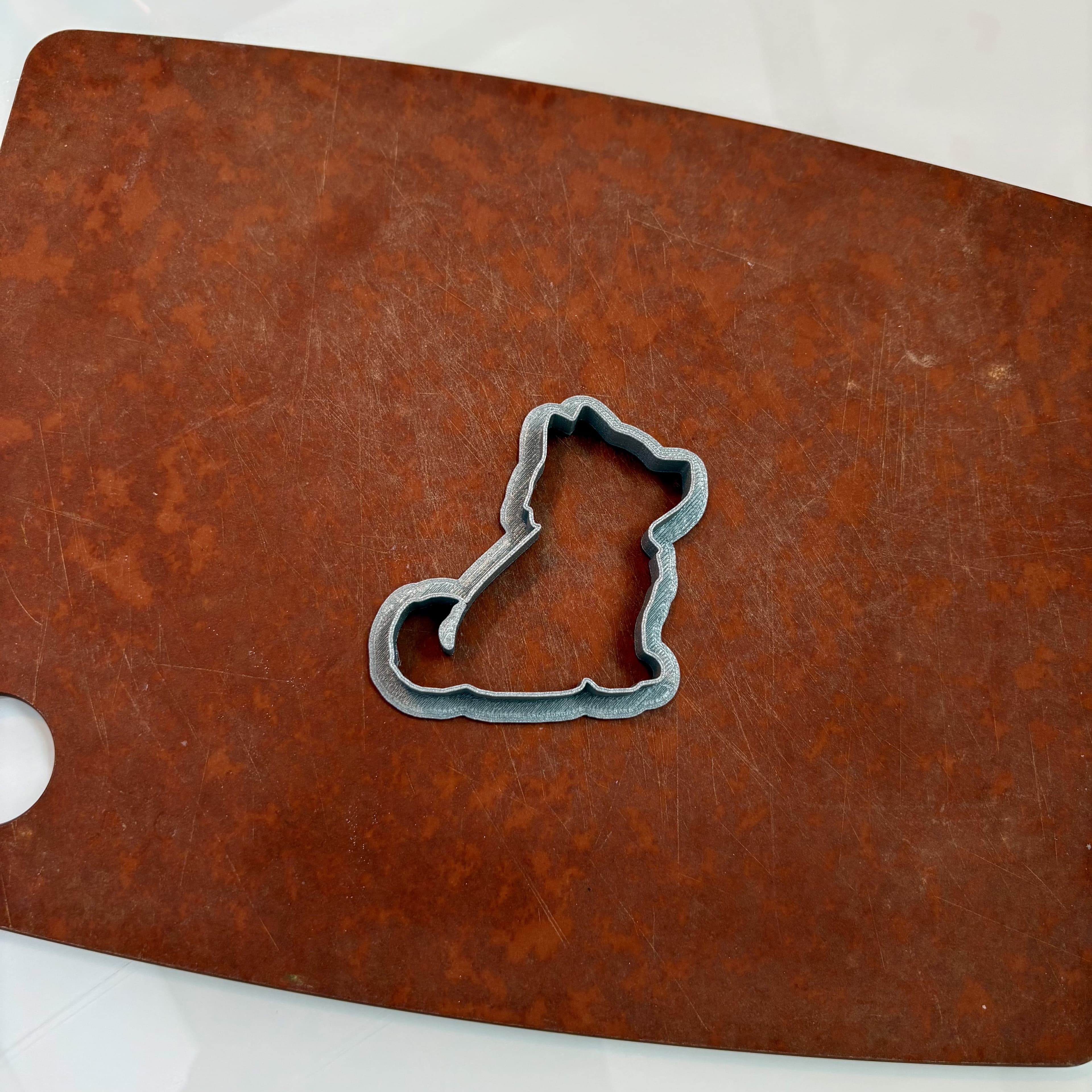 3D-printed dog-shaped cookie cutter on a wooden cutting board
